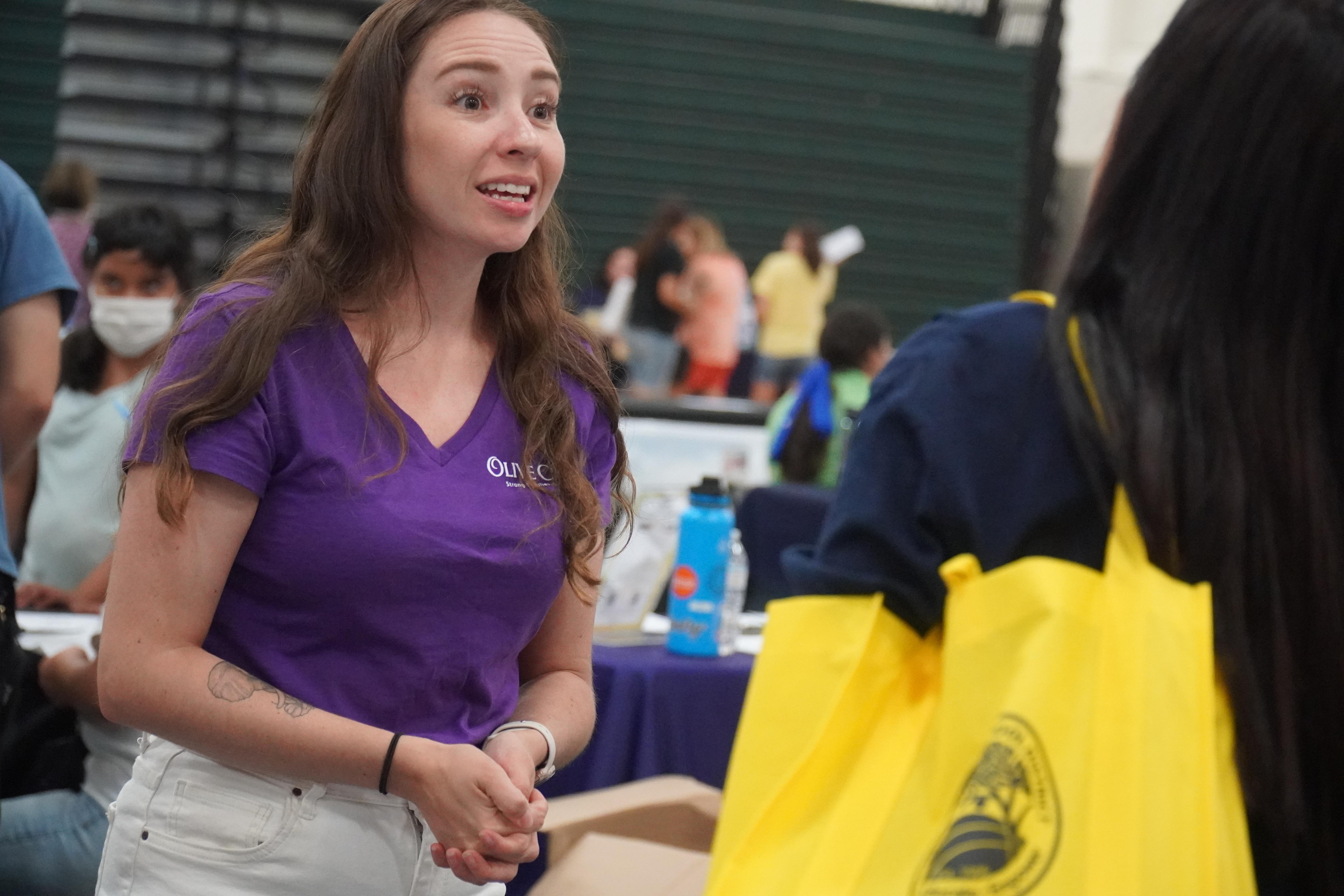 woman in a purple shirt talking to another woman with a table between them